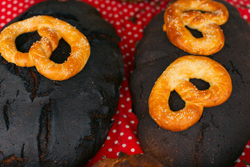 Traditional dark bread loaves topped with golden baked pretzels, displayed on a red polka-dot cloth.