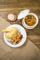 A Chinese herbal chicken soup with chicken, pork, shrimp, mushrooms, and grains served in a rustic setting.