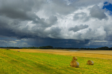 Dramatic rural landscape with hay bales on a field and dark storm clouds approaching across the countryside