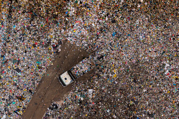Aerial view of a waste truck unloading garbage at a landfill surrounded by massive amounts of mixed plastic and debris.