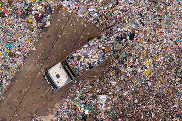 Aerial view of a waste truck unloading garbage at a landfill surrounded by massive amounts of mixed plastic and debris.