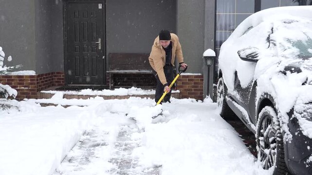 The first snow is falling. A heavy snowfall. A man is shoveling piles of snow from the yard.