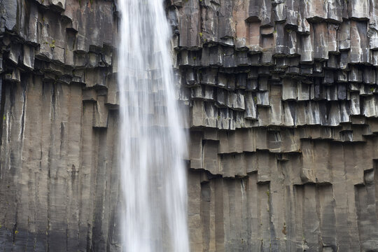 View of a cascading waterfall plunges down a cliff face of dark hexagonal basalt columns, a contrast of textures and tones, Svartifoss, Sveitarf&eacute;lagio Hornafjorour, Iceland.
