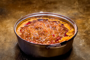 A pot of Sichuan-style hot pot soup actively boiling on an induction stove. Red chilies and steam highlight its intense flavor and heat.