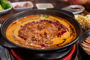 A pot of spicy Chinese hot pot soup base boiling on an induction stove. Red chilies and steam highlight its heat and communal dining appeal.