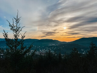 Obraz premium Scenic landscape view featuring silhouetted evergreen trees against a vibrant sunset sky with clouds, showcasing the beauty of nature and tranquility in a mountainous region