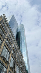 Modern skyscraper with reflective glass facade towers above a low-rise building, showcasing urban architecture against a cloudy sky, emphasizing contemporary design and city life