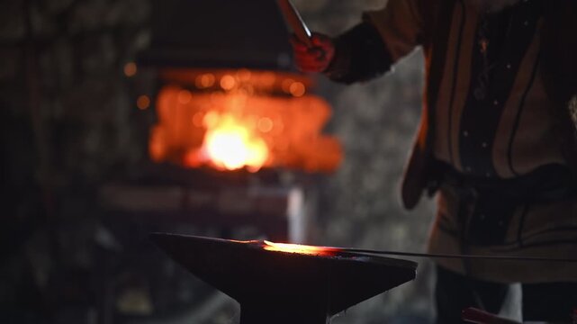 A Viking blacksmith with a white beard and braided hair works intently at a forge, hammering glowing metal on an anvil, with flames flickering in the background of a stone workshop cinematic slow