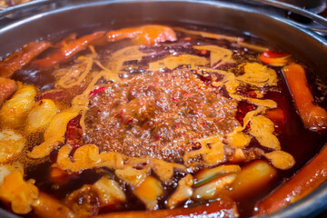 A boiling spicy hot pot on an induction cooker with chili oil and steam rising, set on a red table.