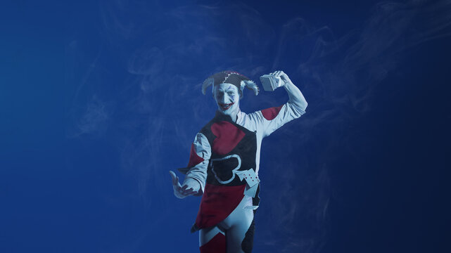 Jester performing dramatic card flourish on blue smoky stage. Concept of entertainment shows, gaming visuals, casino campaigns, character branding, and theatrical promotional content. - Powered by Adobe