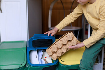 A child places cardboard packaging into a home recycling bin. Concept of early eco education, family sustainability habits and responsible waste management.