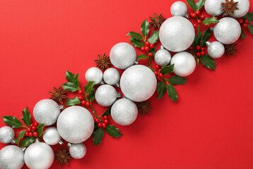 Christmas flat lay composition with white glitter baubles, holly berries, and leaves arranged diagonally on a vibrant red background. Festive holiday decor.