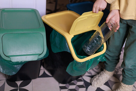 A child puts a plastic bottle into a color-coded recycling bin. Concept of practical eco learning, waste awareness and positive family sustainability routines.
