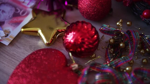 A United Kingdom cost of Christmas concept with a closeup of a bunch of Pound Sterling bank notes and Christmas decorations on a desk.