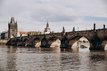 Obraz premium Historic Charles Bridge spanning the Vltava River in Prague under a cloudy sky.