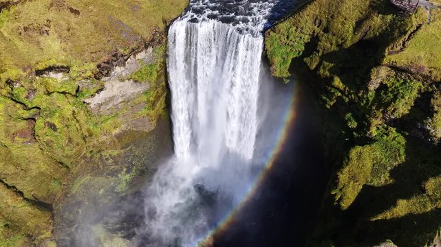 Cinematic top-down drone footage of Sk&oacute;gafoss waterfall in Iceland, showing powerful cascading water, mossy cliffs and mist rising from the impact pool. Dramatic natural landscape captured in high det