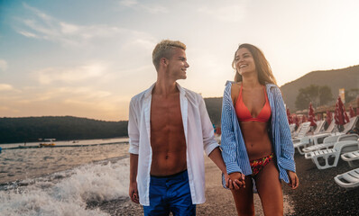 Young beautiful couple walks along the seashore at sunset. Honeymoon. Romantic trip.