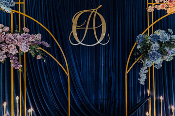 Elegant floral display with blue velvet backdrop featuring golden monogram.