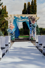 Elegant outdoor wedding ceremony setup with floral decorations and blue drapes under a pergola