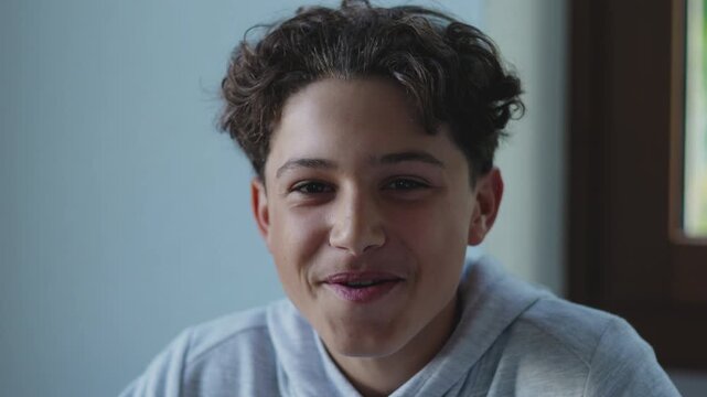 Teen boy smiling warmly indoors with relaxed joyful expression, creating lighthearted and genuine moment that conveys happiness and openness in calm home environment