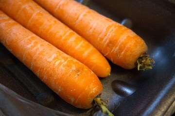 3 whole carrots placed on a black paper tray in close-up, ideal as a vegetable background.