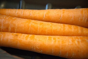 3 whole carrots placed on a black paper tray in close-up, ideal as a vegetable background.