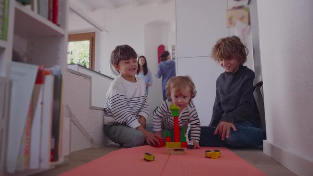 Toddler arriving at play area and casually knocking over siblings&rsquo; block build creating authentic family moment filled with gentle interruption natural curiosity