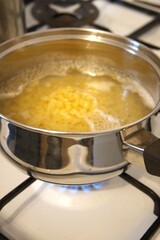 Small shell pasta cooking in water inside a cooking pan in close-up, showing homemade soup preparation.