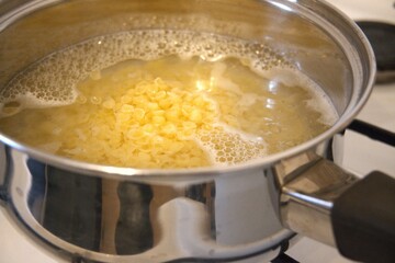 Small shell pasta cooking in water inside a cooking pan in close-up, showing homemade soup preparation.