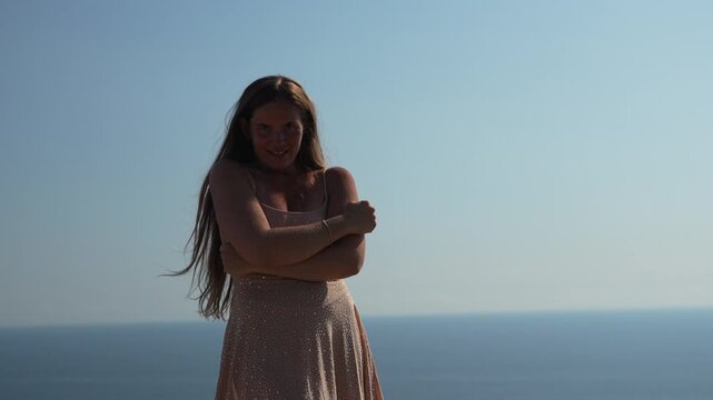 Woman posing ocean, in a sparkling dress expresses herself confidently against a clear blue sky