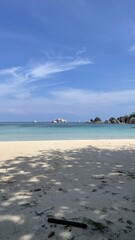 Obraz premium Serene tropical beach with white sand, clear turquoise water, and distant islands under a blue sky.