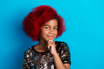 Young girl with bright red hair wearing a sparkling sequined top smiles against bold blue background