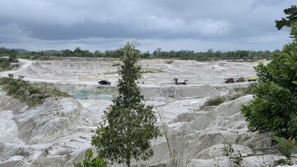 An expansive open-pit mining operation with white mineral deposits and heavy machinery under an overcast sky.