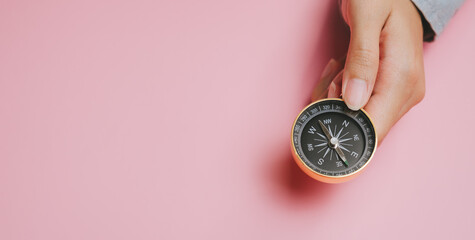 Hand holding compass on pink background, navigation tool for direction and travel concept with copy space for text or design