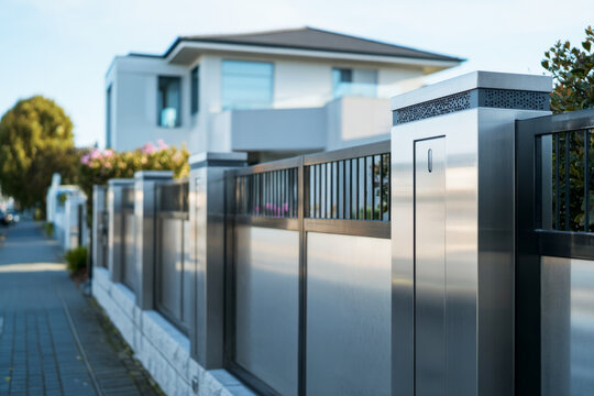 Modern fence showcases advanced facial recognition technology and smartphone-controlled access. The sleek metal panels reflect light in a residential setting, enhancing security and style