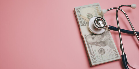 Medical cost concept with stethoscope on stack of hundred dollar bills on pink background,...