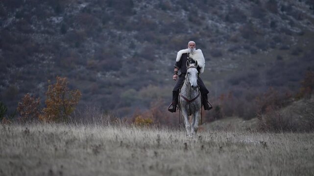Elderly Viking warrior in fur cloak riding gray horse across open field at sunrise, mountains and distant cross behind him, moody cinematic Norse atmosphere cinematic slow motion 