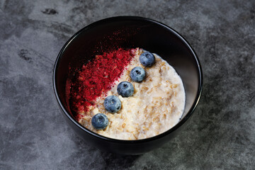 Oatmeal Bowl With Blueberries And Red Berry Powder On Dark Ceramic Plate