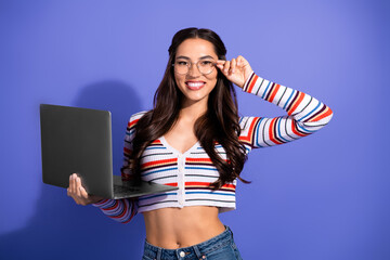 Young woman with glasses holding laptop smiling in striped top against violet background for fashion lifestyle stock photo