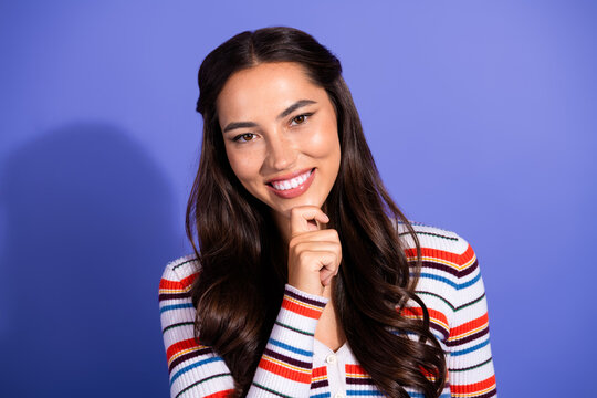 Young woman with long brunette hair smiles in a colorful striped sweater against a violet background perfect for fashion lifestyle advertising campaigns
