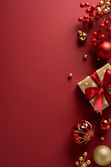Fototapeta premium A vertical festive holiday scene featuring a wrapped gift, red ribbon bow, and gold ornaments on a deep red backdrop ready for Christmas and New Year celebration greetings and seasonal decor