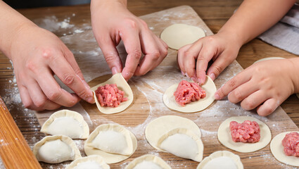 Hands of adult and child making homemade dumplings with raw meat filling on wooden board, traditional family cooking process with flour and dough circles
