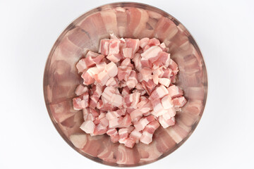 An overhead studio shot of a metal mixing bowl filled with raw pork belly, cut into small, uniform cubes of pink meat and white fat, set against a light background