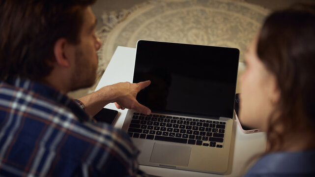 Man pointing at laptop screen explaining information to woman at home. Concept of digital guidance, shared learning, troubleshooting help, and collaborative decision-making in everyday home routine.