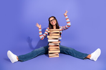Happy young woman student sits with a tall stack of books on a purple background