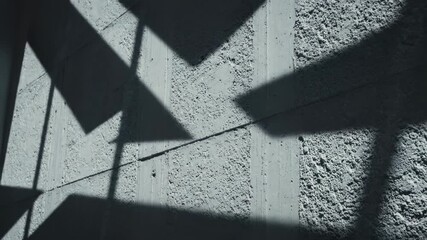 Dramatic slow pan across a rough concrete wall as sharp architectural light beams shift and move creating a dynamic shadow pattern building, moody, dramatic