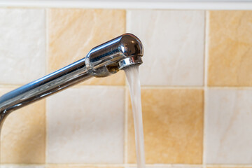 Stainless steel kitchen tap or faucet with water running in front of earthy coloured tiles