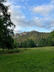 Sunny mountain ridge rising above a green meadow with trees and blue sky.