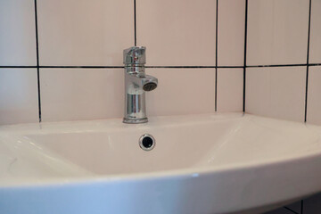 Fototapeta premium Close Up Of A Metal Mixer Tap In A Bathroom With White Tiled Walls. Concept Of Hygiene, Plumbing, And Cleanliness.