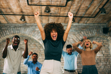Excited diverse business team enthusiastically raises their arms and cheers, celebrating success in a modern office